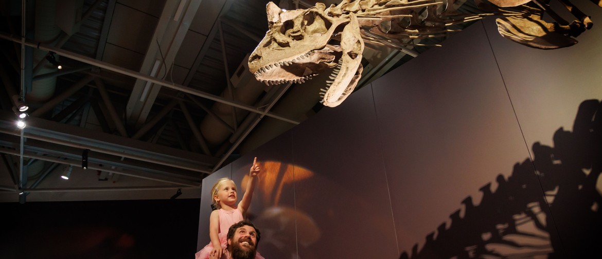 Person carrying child on their shoulders. Child pointing a fossil of a dinosaur with a long head.