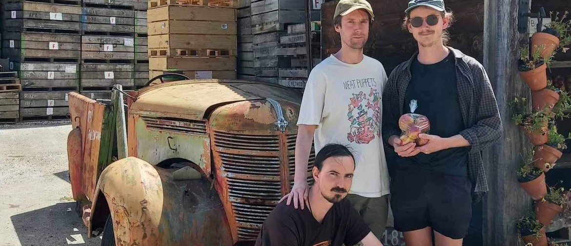 Member's of three piece Pōneke band Oddish in front of a rusty tractor and with a bag of apples.