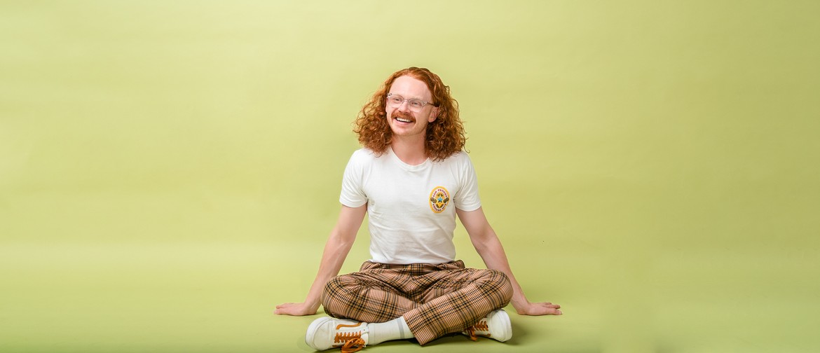 performer Nick Robertson sits cross-legged in front of a yellow background
