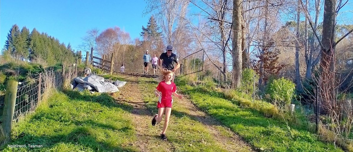 Young girl runs down a farm track during the annual Waimea Harriers Scarecrow Scamper, followed by  3 adults passing through a farm gate in rural Tapawera