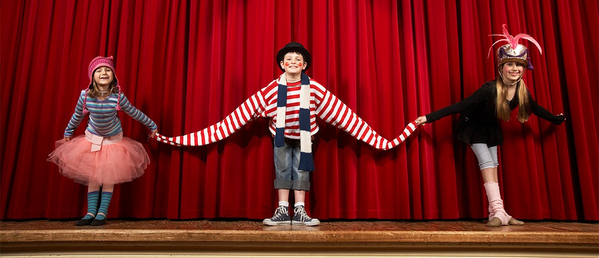 Take A Bow! 5-Day Theatre Holiday Programme Three smiling kids, in costume, bowing on stage, with red curtain behind them